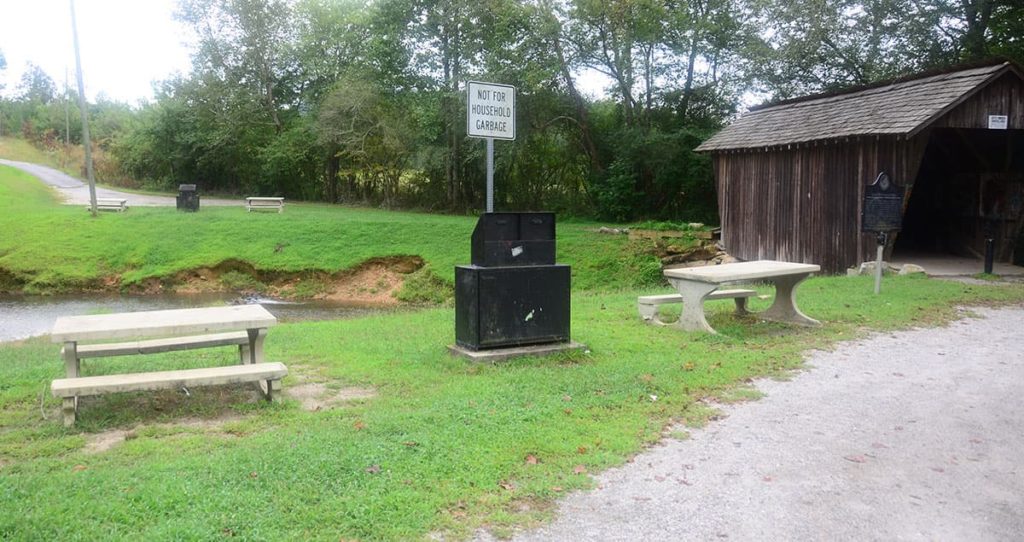 Picnic tables and trash receptacles next to the covered bridge.